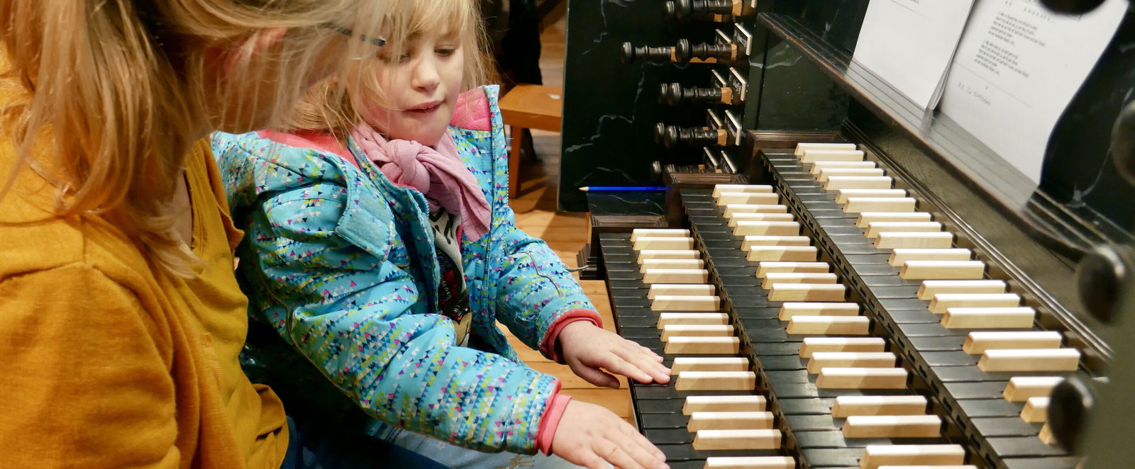Eine erwachsene Person sitzt mit einem Kind an den Tasten einer Orgel.