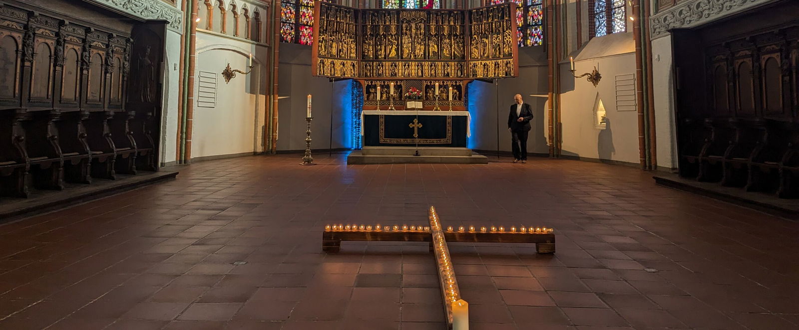 Blick in den Altarraum einer Kirche. Auf dem Boden bilden Kerzen ein Kreuz. Links und rechts des Altars sind die Wände blau beleuchtet.