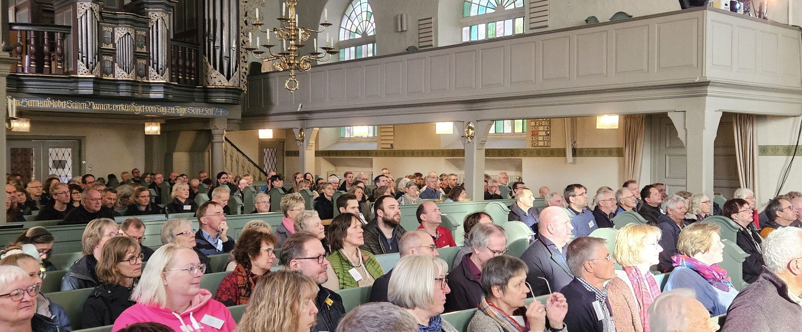 In Kirchenbänken sitzen viele Menschen. Im Hintergrund eine barocke Orgel.
