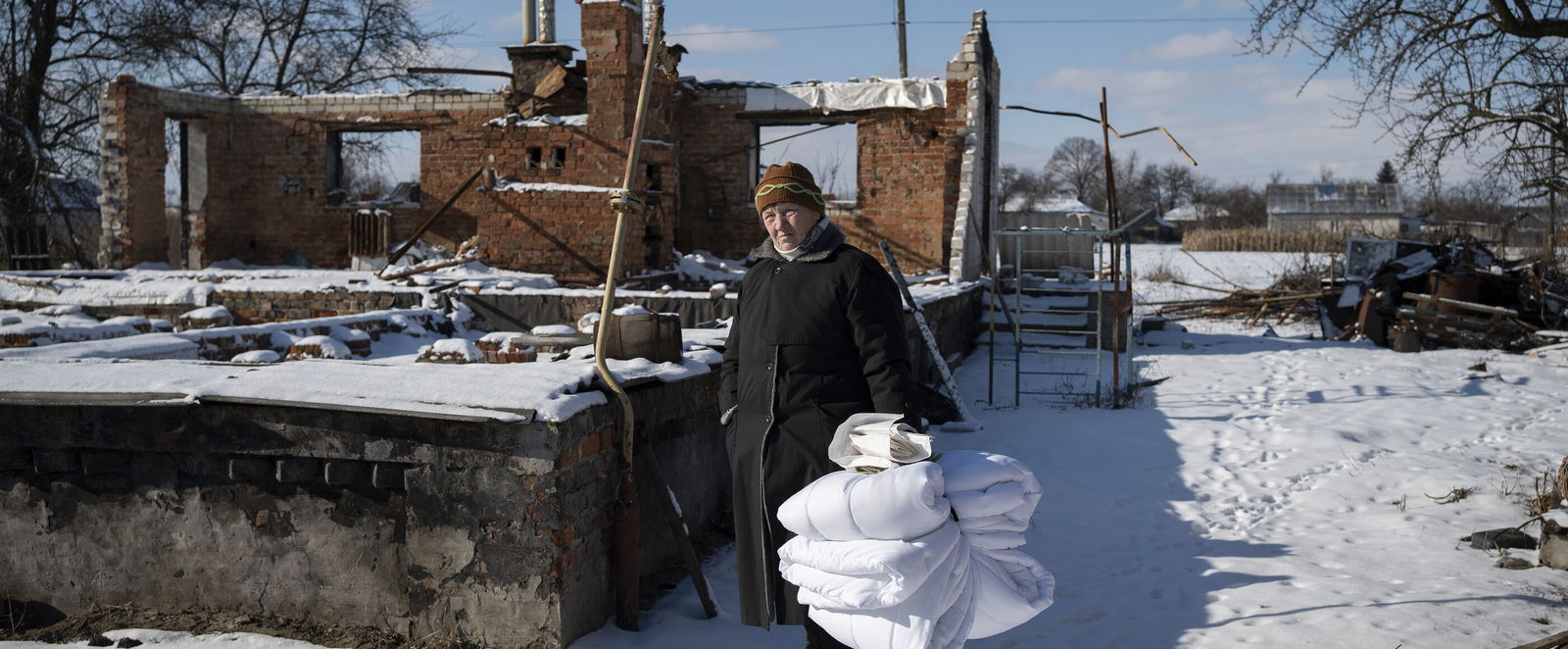 Eine Person steht mit zusammengebundenen Decken im Schnee zwischen Ruinen.