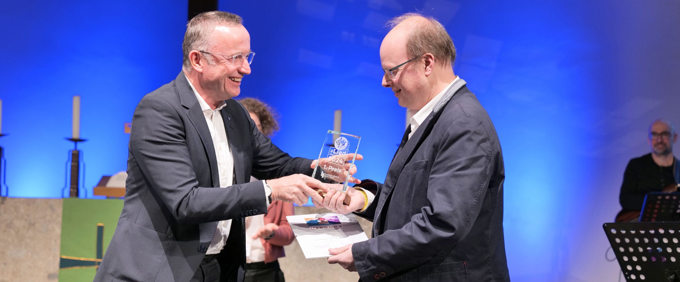Ein Mann bekommt auf der Bühnen einen Preis überreicht.