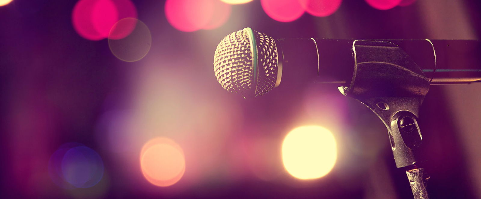ein Mikrofon auf einer Buehne. Im Hintergrund sieht man Scheinwerferlicht.