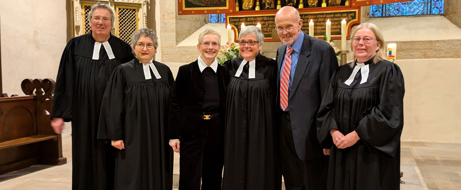Menschen in Talaren vor einem Kirchaltar