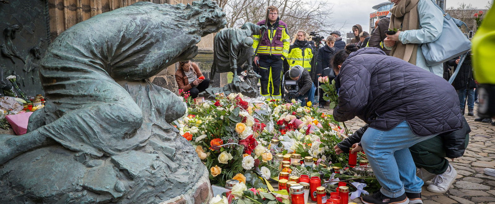 Viele Menschen legen Blumen am Eingang einer Kirche nieder.