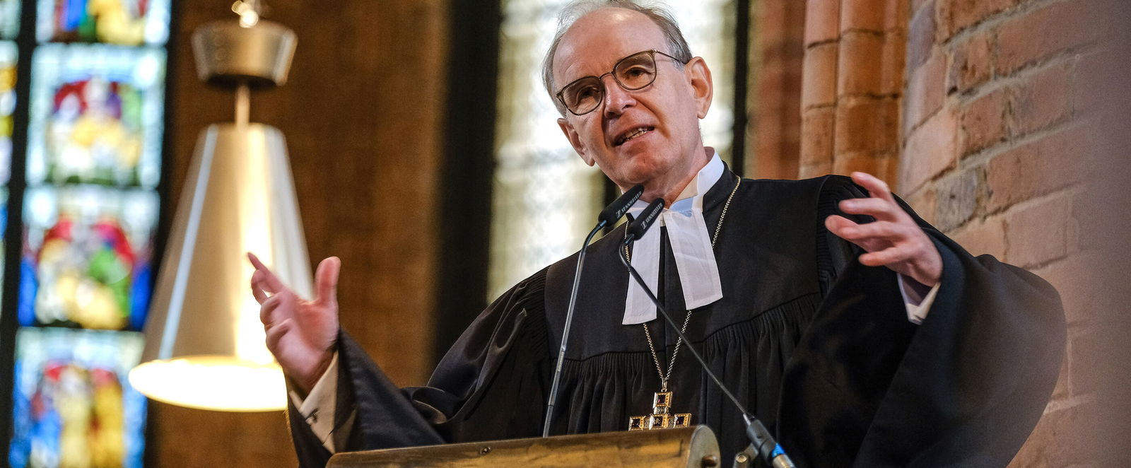 Eine als Mann lesbare Person im Talar steht auf einer Kanzel und predigt.