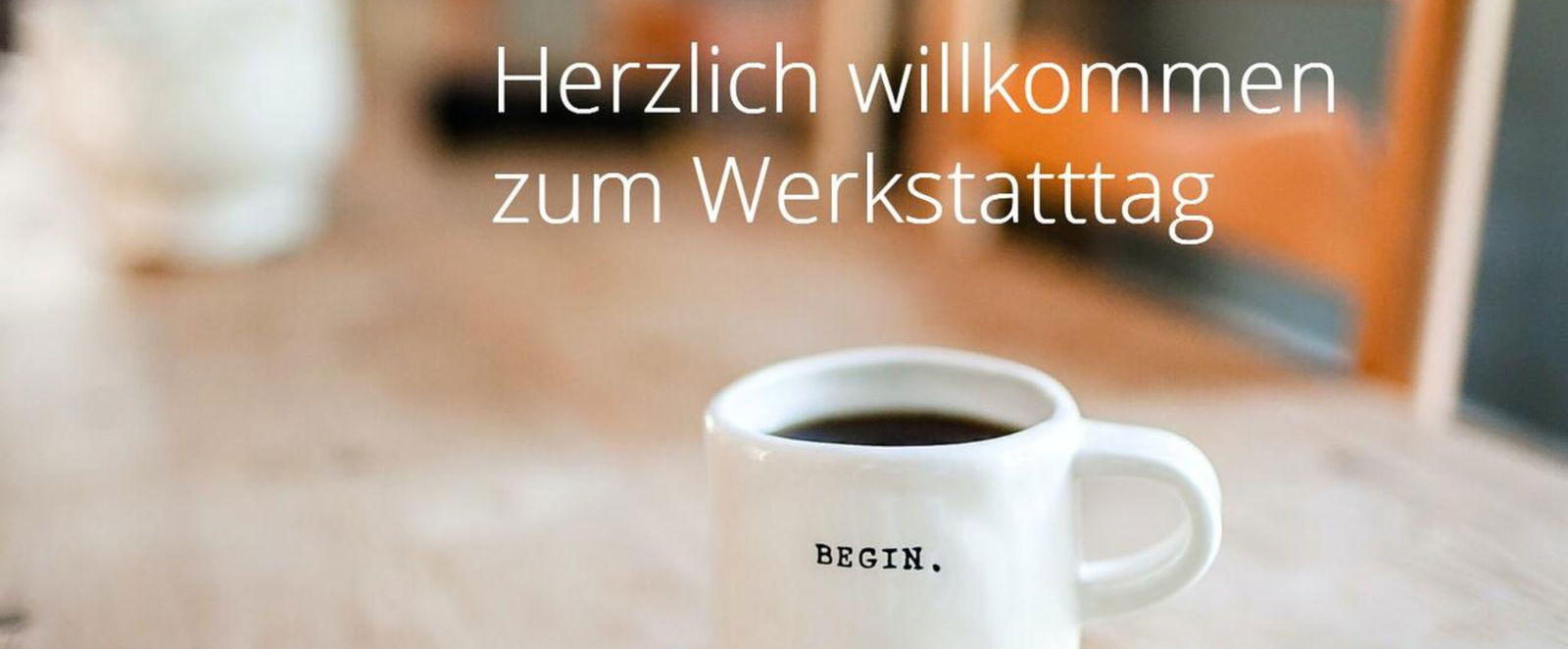 Auf einem Holztisch steht ein weißer Becher mit der Aufschrift "Begin"; in die Grafik eingebaut ist der Text "Herzlich willkommen zum Werkstatttag"