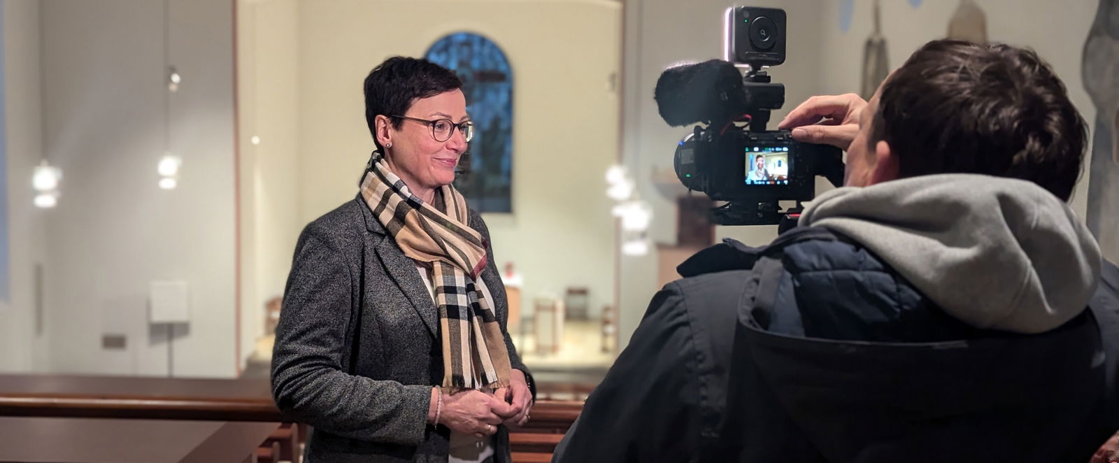 Eine als Frau lesbare Person gibt ein Interview und wird dabei gefilmt.