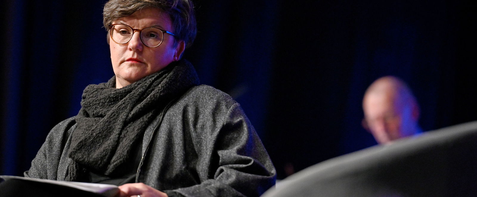 Eine Frau mit kurzen Haaren vor einem dunklen Hintergrund.