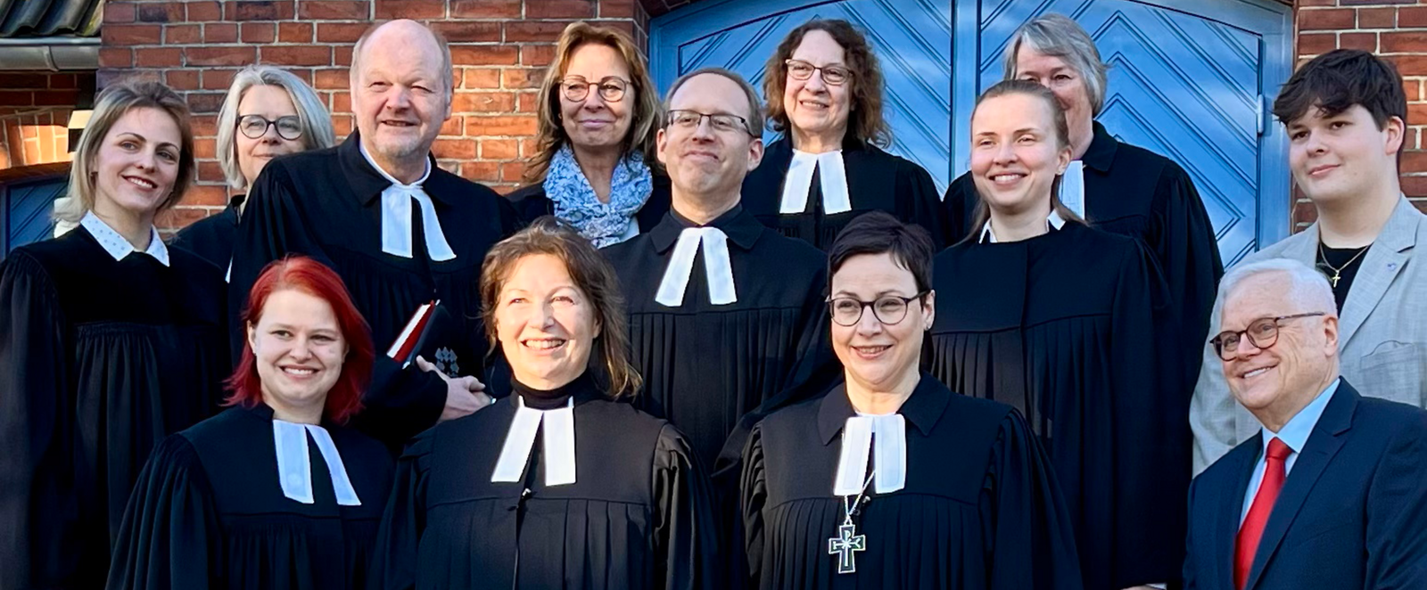 Mehrere Personen, teils in Talaren, stehen vor einer blauen Holztür in einem großen Gebäude.