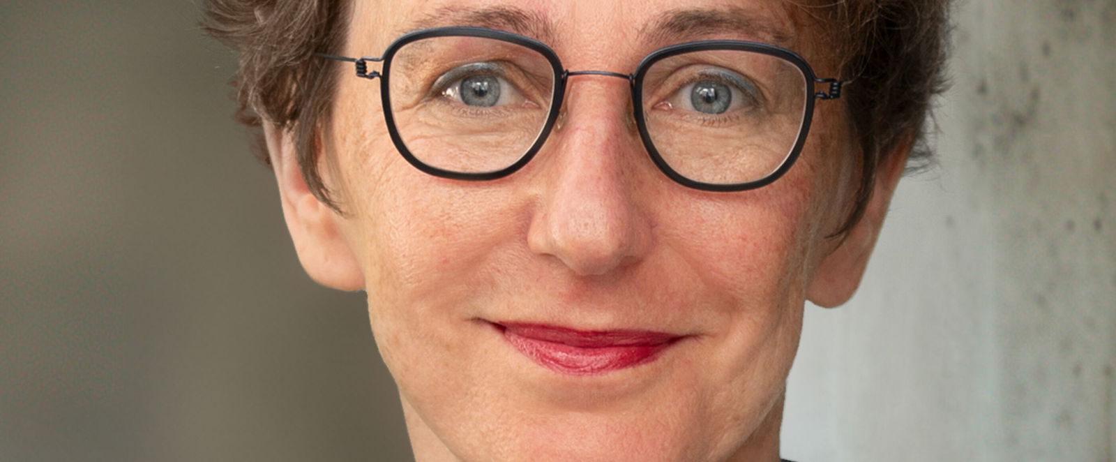 Eine als Frau lesbare Person mit Brille und kurzen lockigen Haaren.