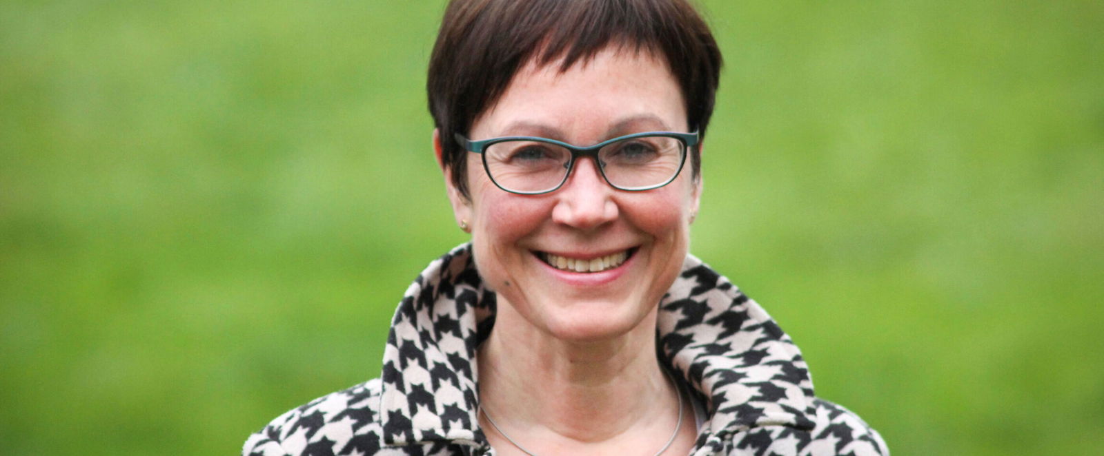 Eine als Frau lesbare Person mit kurzen Haaren und Brille.