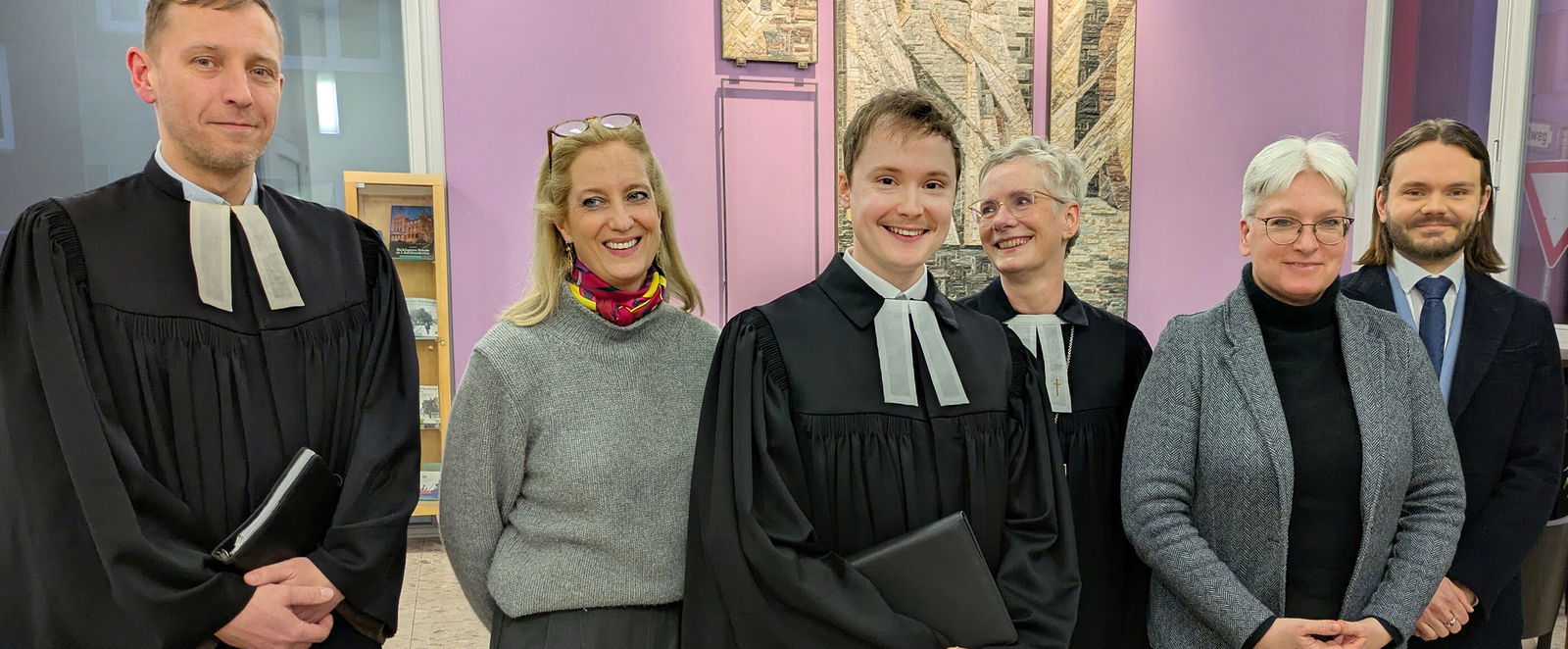 Eine Gruppe aus weiblich und männlich lesbaren Personen posieren als Gruppe, zwei davon im Talar.