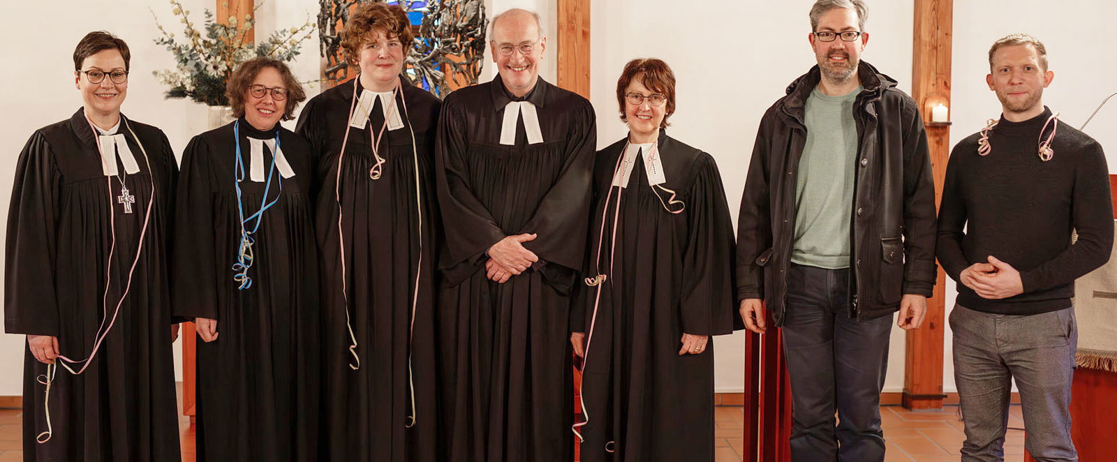 Eine Gruppe aus weiblich und männlich lesbaren Personen posiert im Talar.