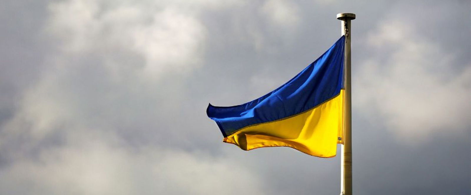 Eine blau-gelbe, ukrainische Flagge weht an einem Mast vor dunklen Wolken.