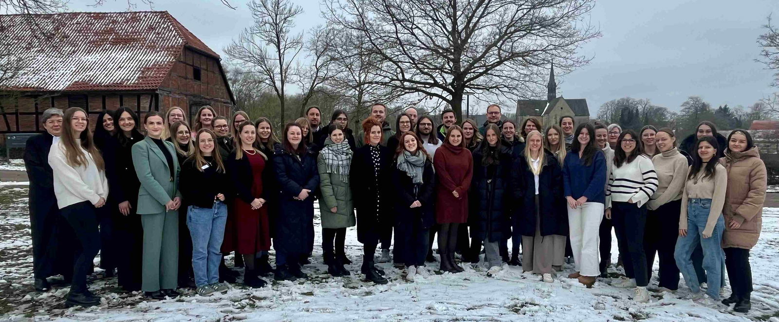 Mehrere Menschen stehen auf einer verschneiten Fläche, im Hintergrund ein spitzer Kirchturm vom Kloster Loccum.