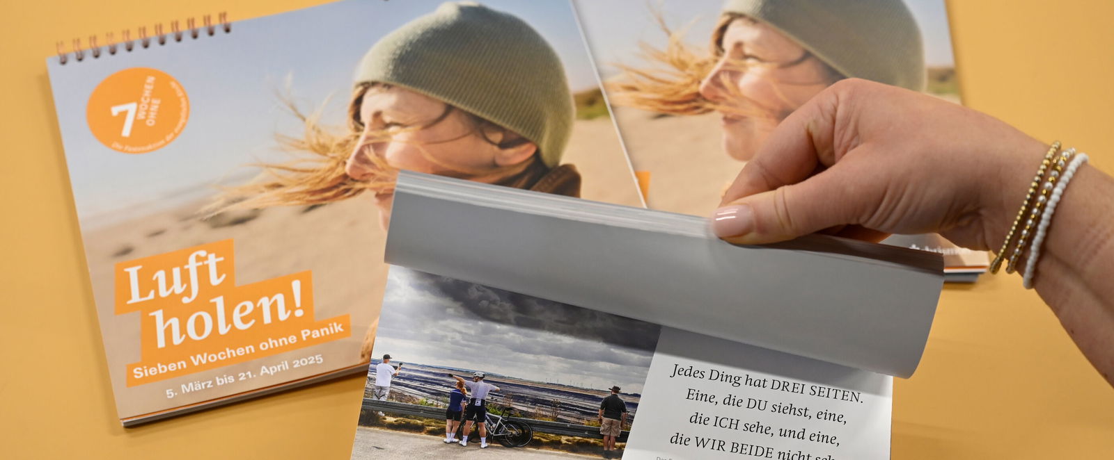Auf einem orangenen Hintergrund liegen Kalender mit der Aufschrift "Luft holen". Jemand blättert durch einen hindurch.