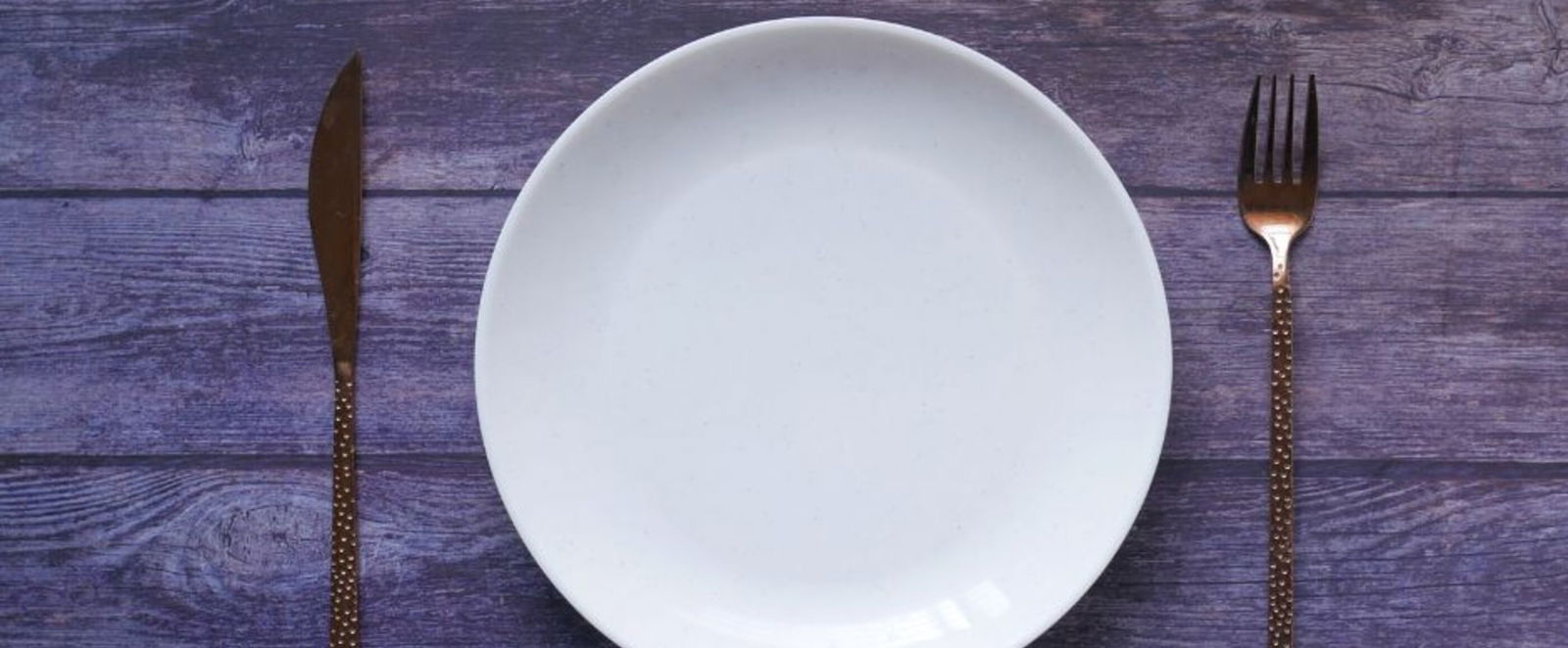 Ein weißer, leerer Teller mit Besteck auf einem grauen Untergrund.