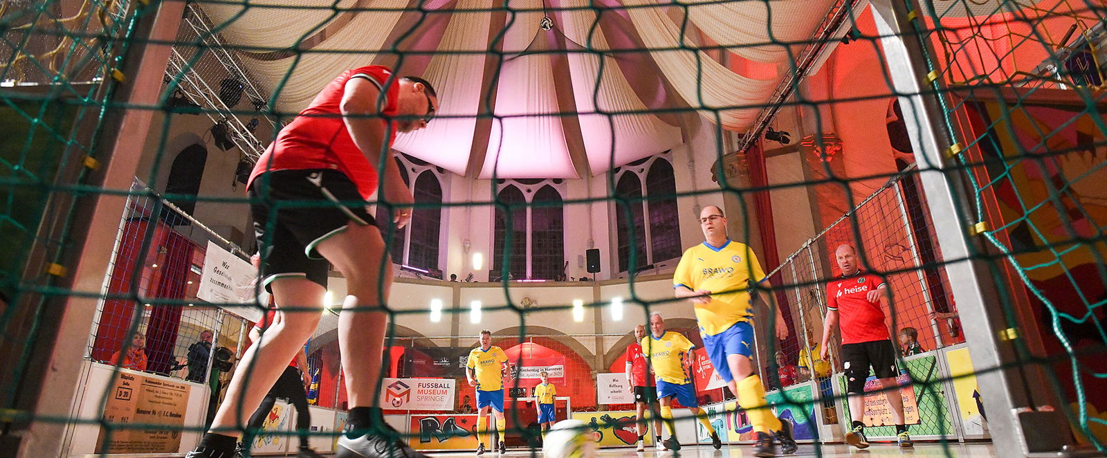 In einer Kirche spielen als Männer lesbare Personen auf einem Indoor-Feld Fußball.