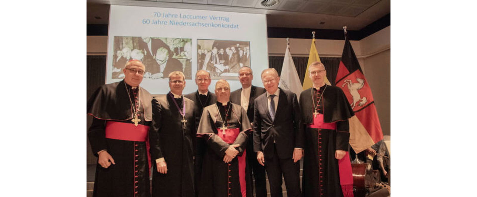 Eine Gruppe Männer in festlicher Kleidung wird auf einer Bühne fotografiert.