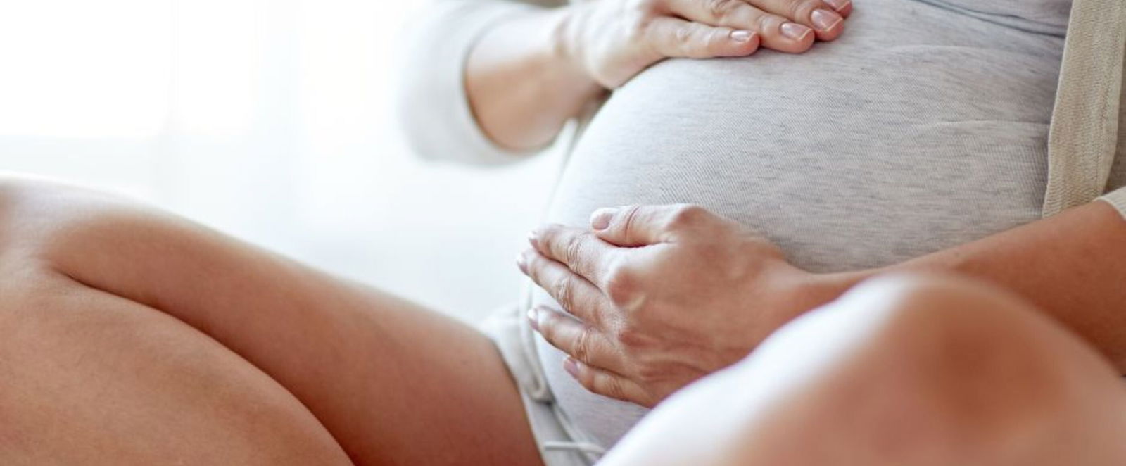 Eine Frau mit Babybauch sitzt im Schneidersitz und hält ihren Bauch.