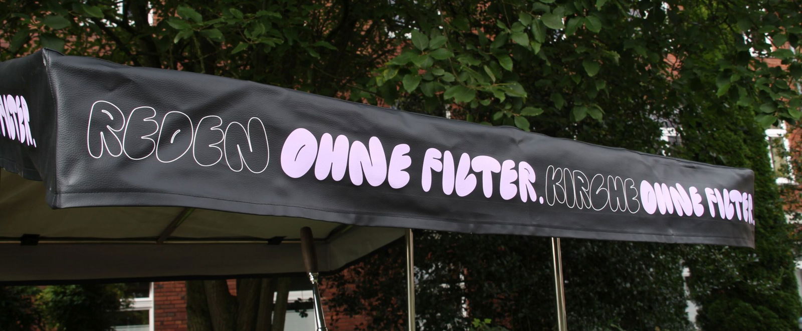 Auf einem schwarzen Sonnenschirm eines Lastenrades steht "Reden ohne Filter, Kirche ohne Filter"