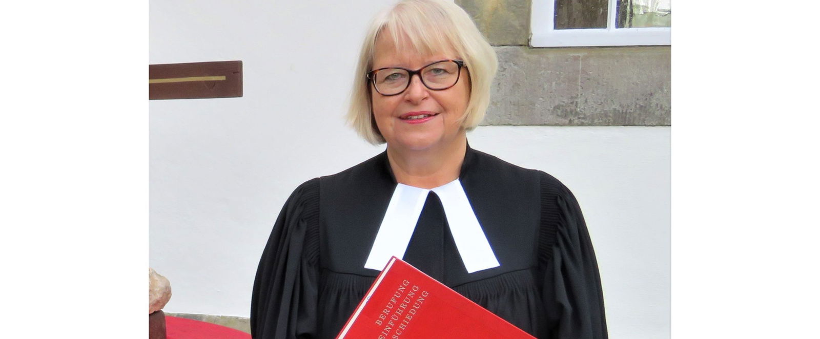 Eine Frau im Talar mit einem roten Buch.