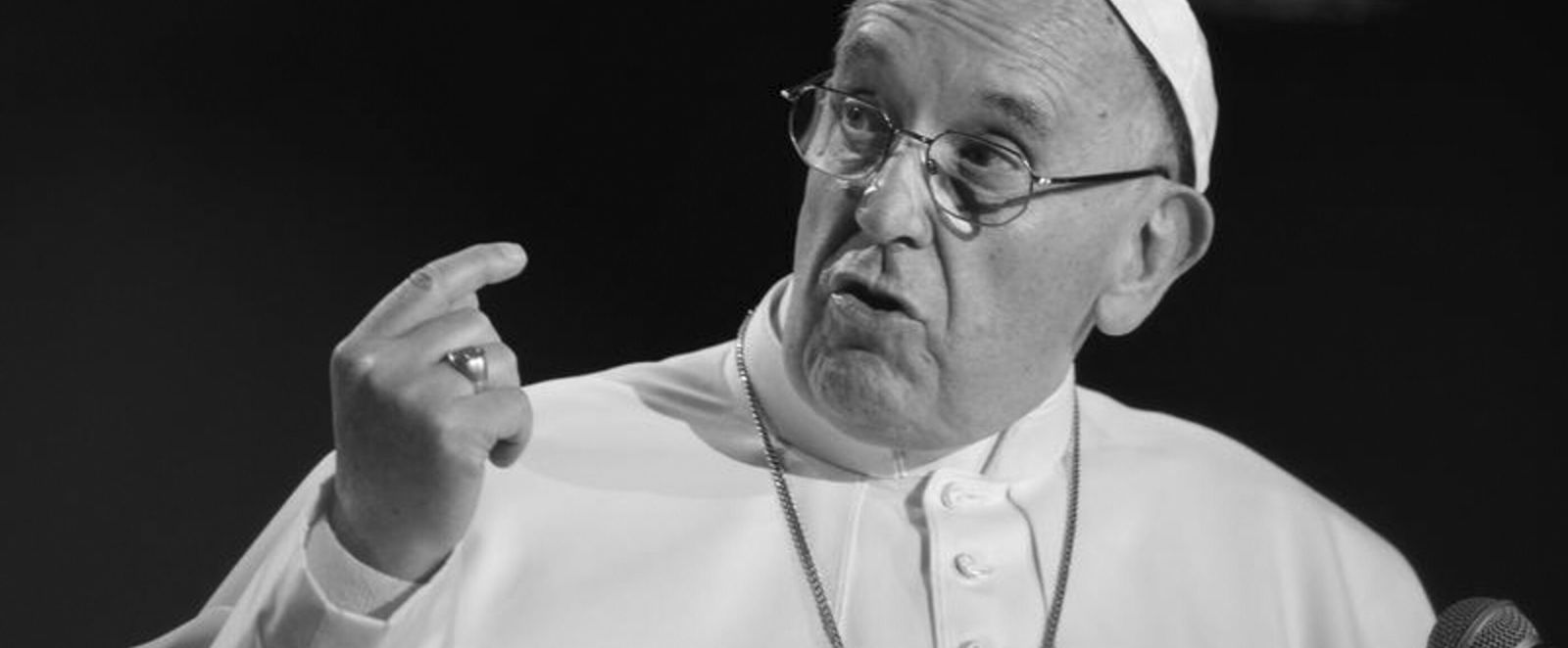 Eine männlich zu lesende Person mit Brille hebt während einer Rede die Hand.