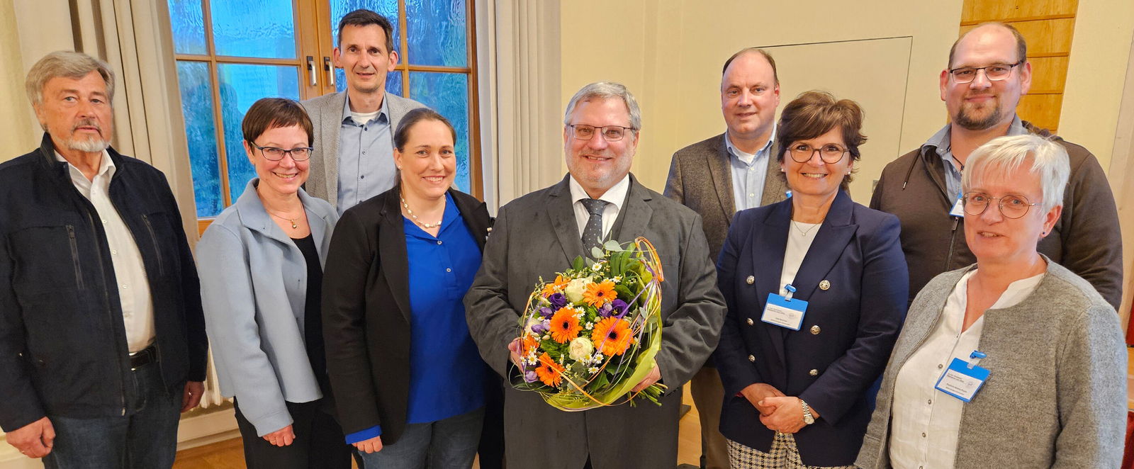 Eine Gruppe von als Frauen und Männer lesbare Personen, eine als Mann lesbare Person hält einen Blumenstrauß.
