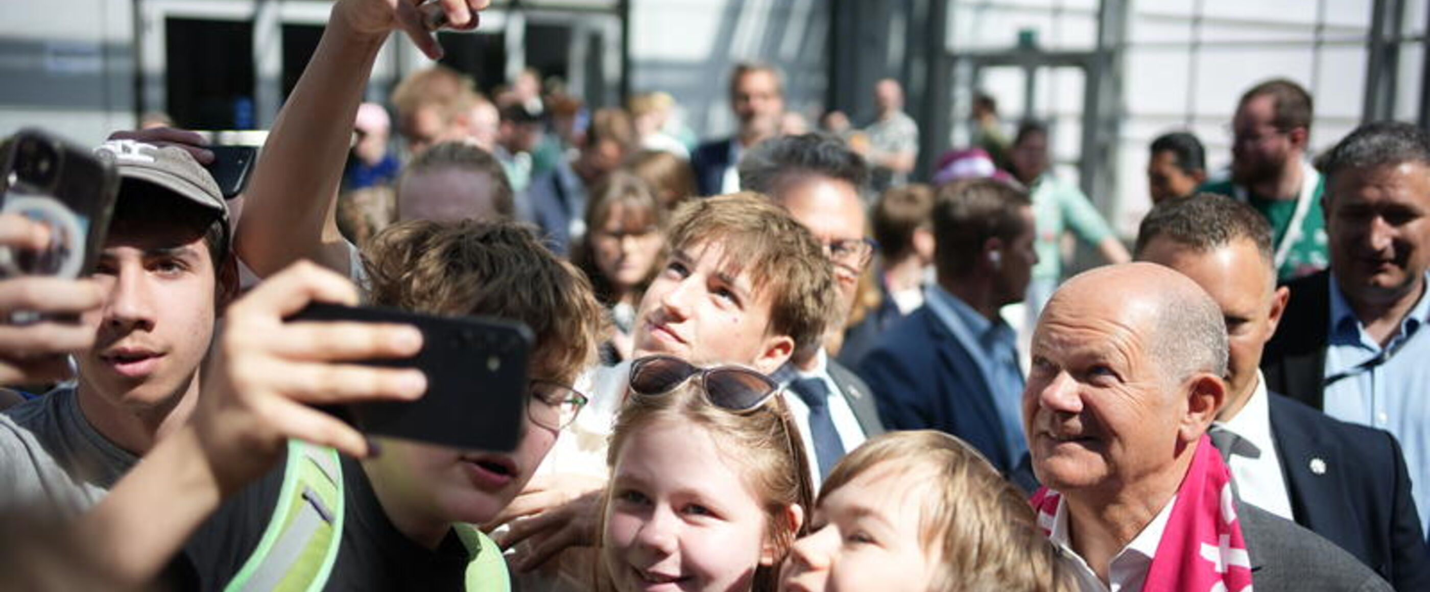 Eine Gruppen von Personen unterschiedlichen Alters macht ein Selfie mit einer männlich zu lesenden Person.