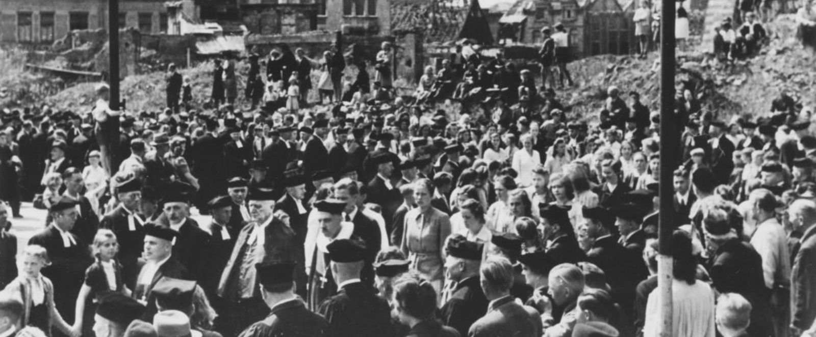 Geistliche ziehen, umringt von Menschen, durch eine zerstörte Stadt (Hannover).