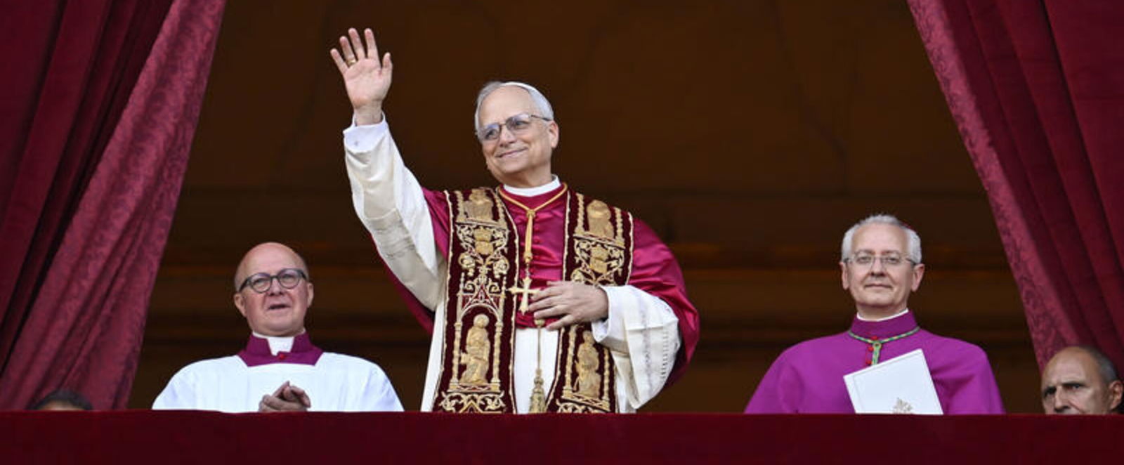 Eine ältere männlich zu lesende Person steht auf einem Balkon und winkt.