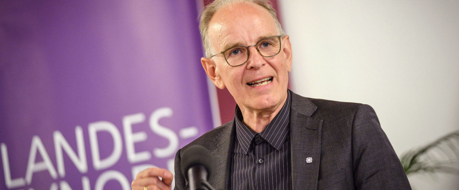 Eine als Mann lesbare Person mittleren Alters spricht in ein Mikrofon.