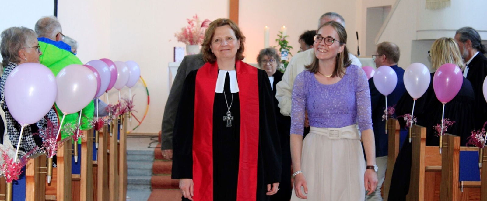 Zwei als Frauen lesbare Personen gehen durch den Mittelgang einer Kirche, links und rechts schweben Luftballons.