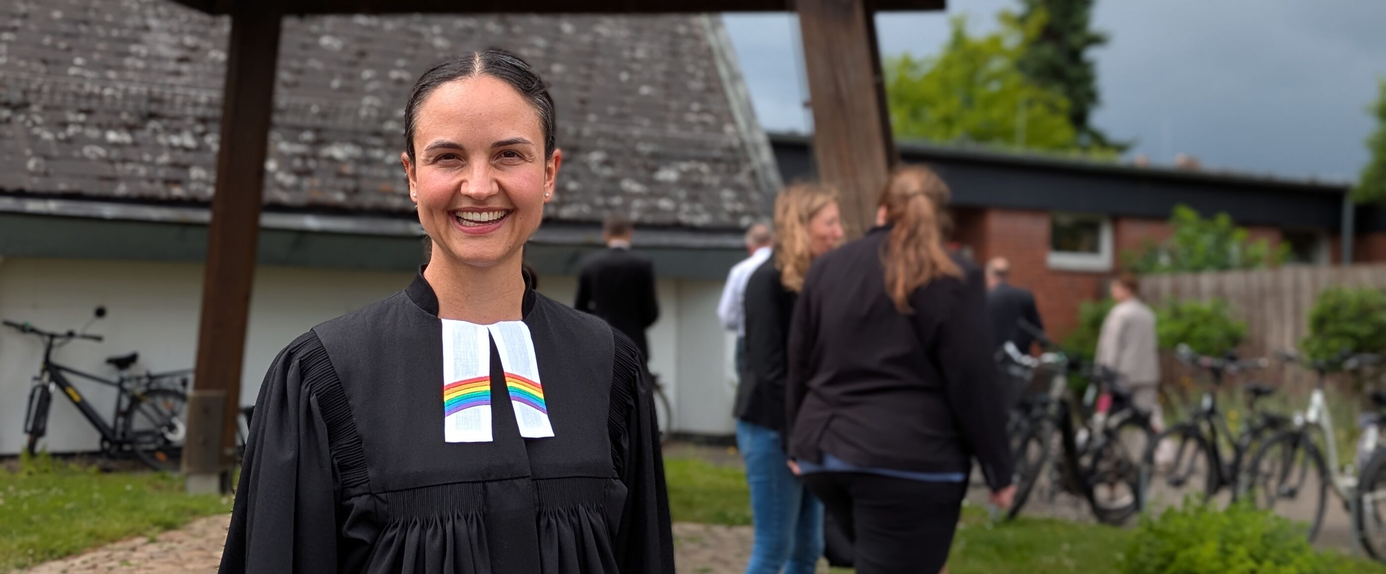 Eine weiblich gelesene Person im Talar steht im Freien und lächelt.