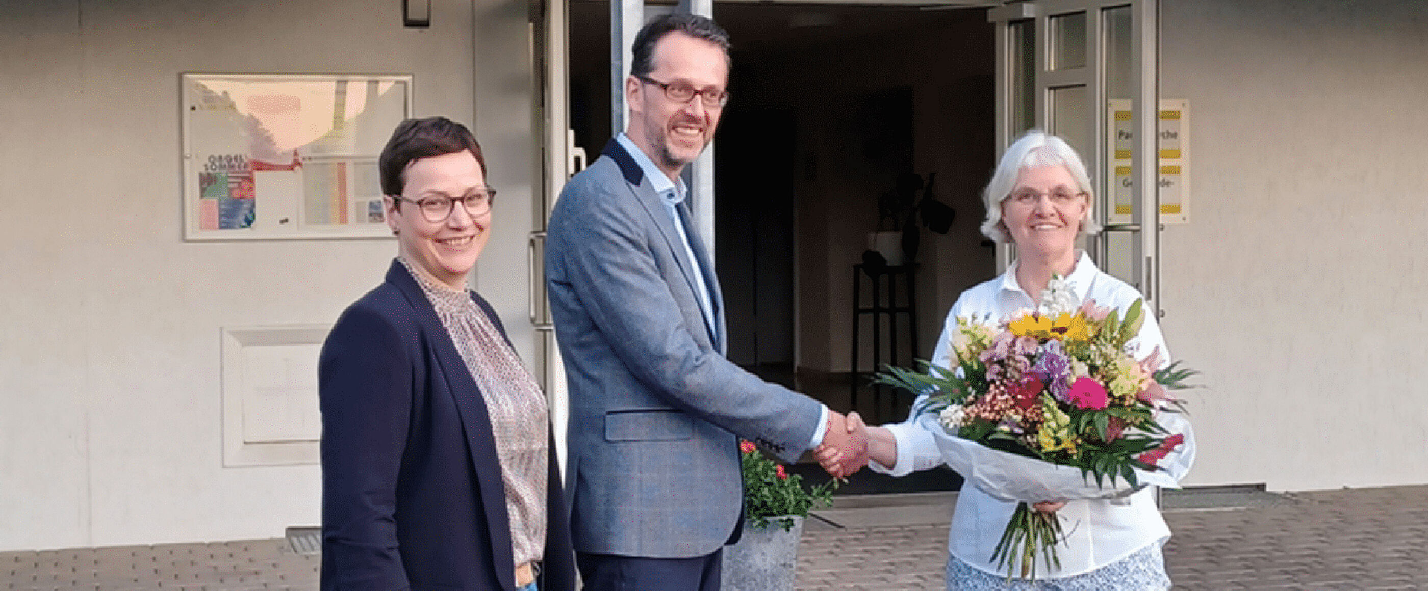 Eine als Mann lesbare Person nimmt Glückwünsche zweier als Frauen lesbare Personen entgegen.