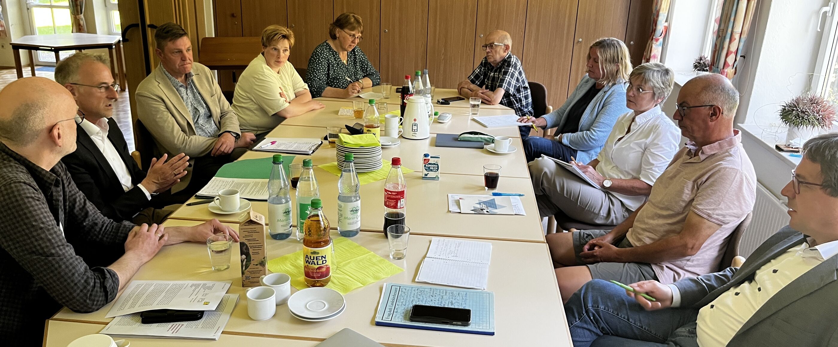 An einem langen Tisch sitzt ein Dutzend Menschen und diskutiert miteinander.