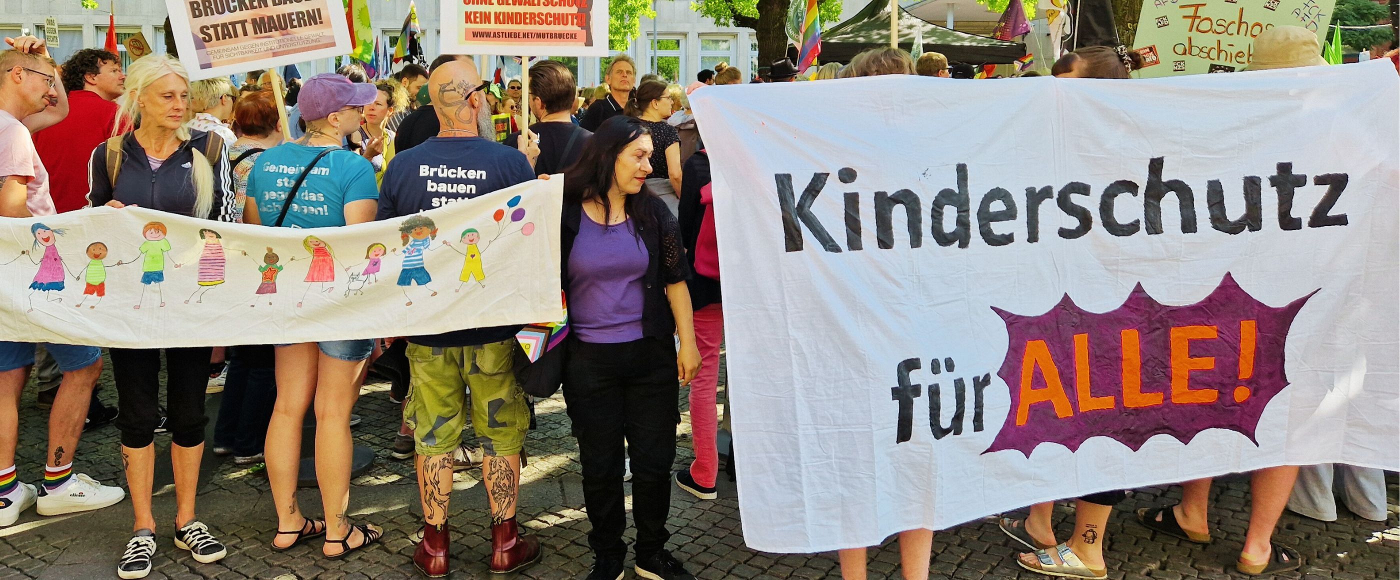 Menschen auf einer Demonstration mit einem Banner, darauf steht Kinderschutz für alle.