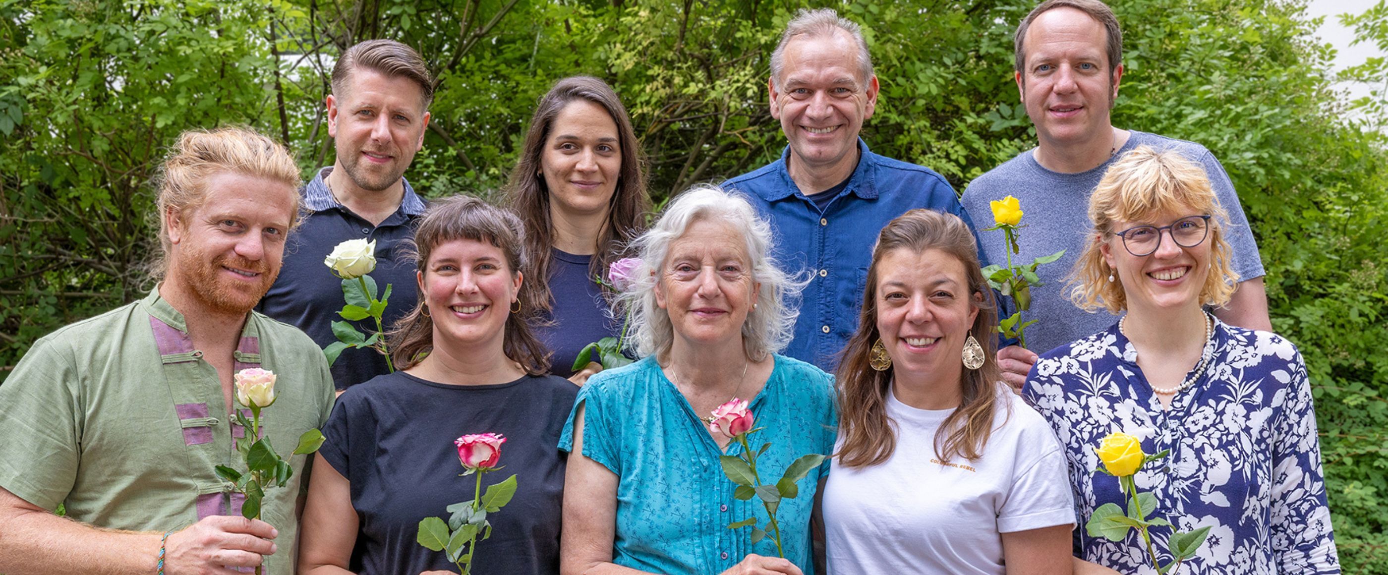 Ein Gruppenfoto, die Personen lächeln und halten Blumen