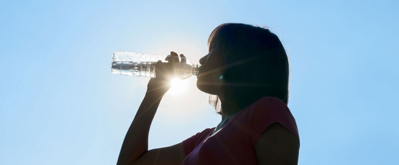 Eine als Frau lesbare Person trinkt aus einer Wasserflasche.