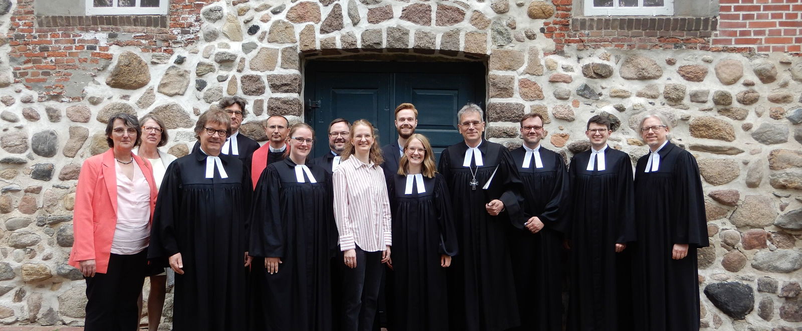 Mehrere Menschen, die meisten im Talar, vor einer Kirche aus großen Steinen. 