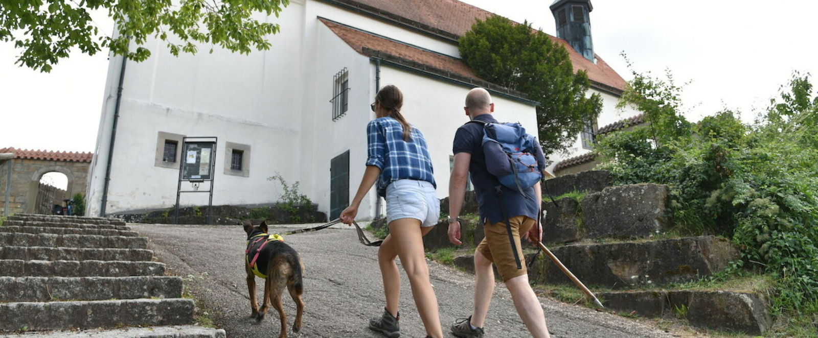 ein Paar mit Hund geht auf eine Kirche zu