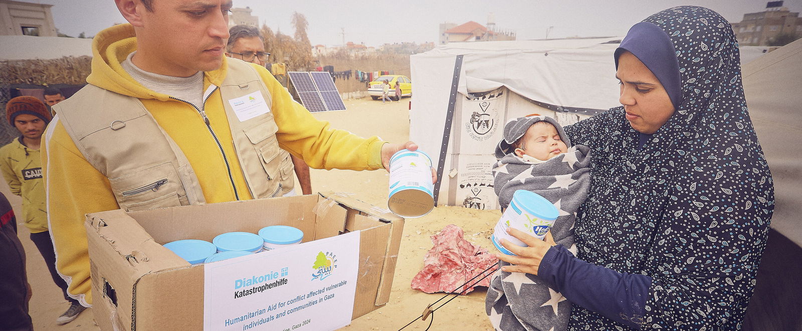 Eine Person gibt eine Dose an eine Person mit einem Kind auf dem Arm.