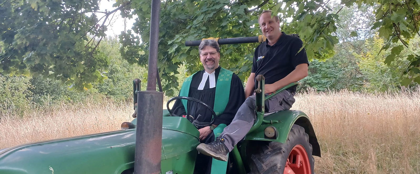 Zwei Männer auf einem Trecker, einer trägt einen Talar.