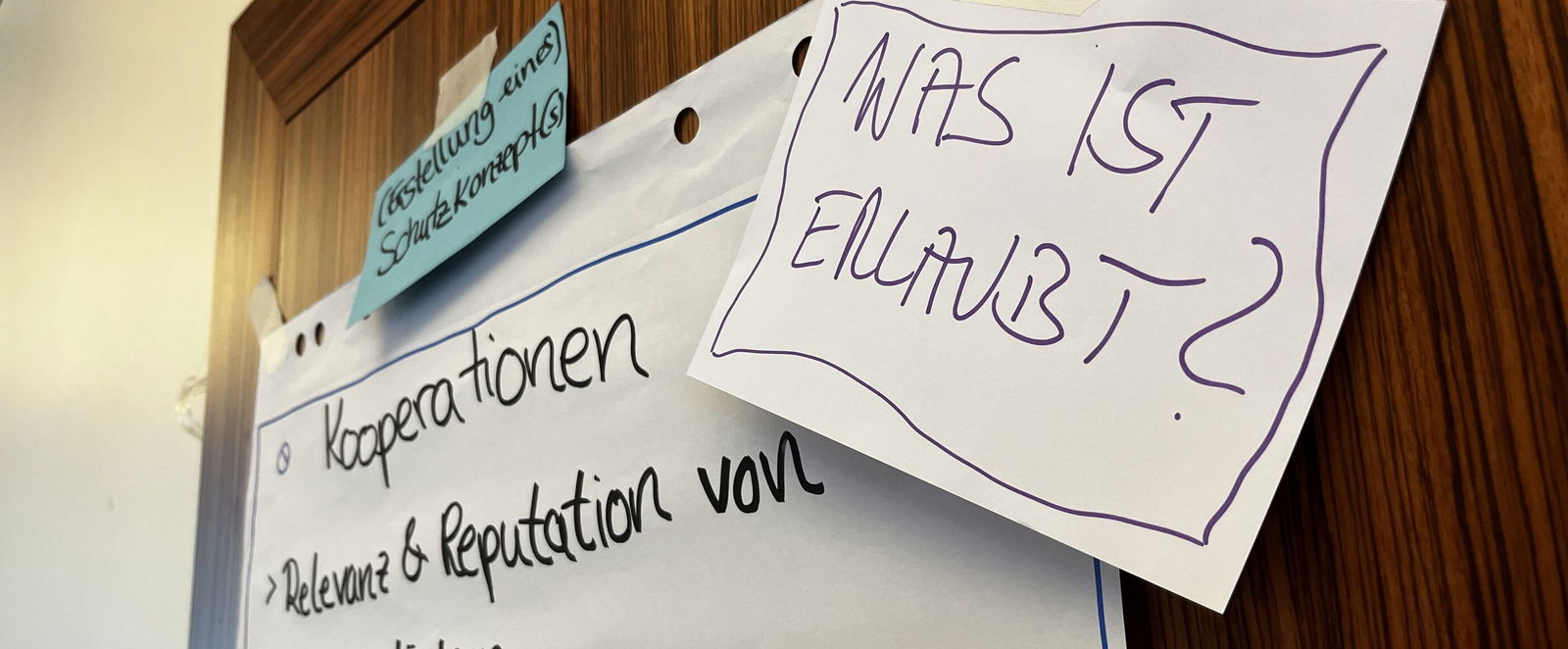 mehrere Papier-Zettel kleben an einer Wand. Darauf ist unter anderem folgender Text zu lesen: Was ist erlaubt?