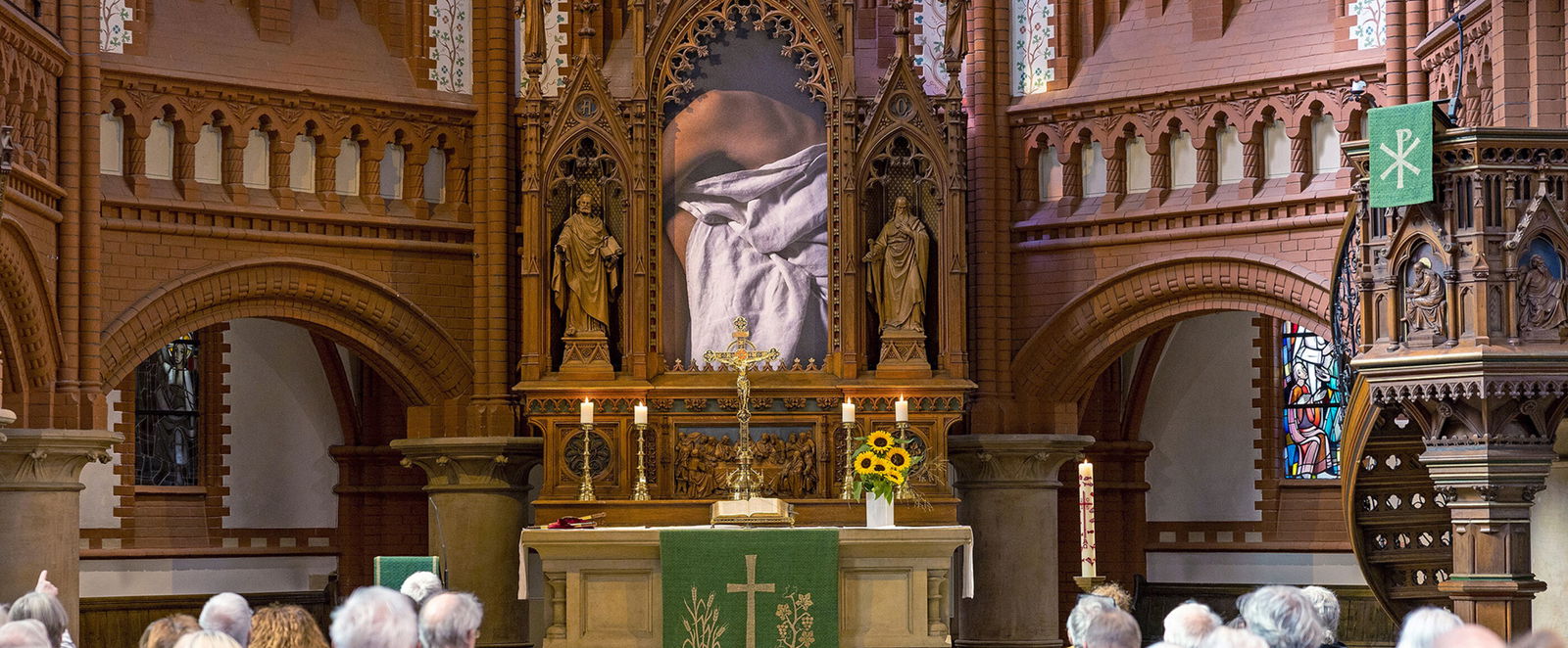 Eine Gemeinde schaut in einer Kirche auf einen Altar mit einem halb verhängten Bild.