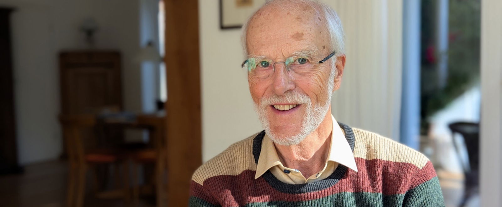 Eine als Mann lesbare ältere Person im Wohnzimmer.