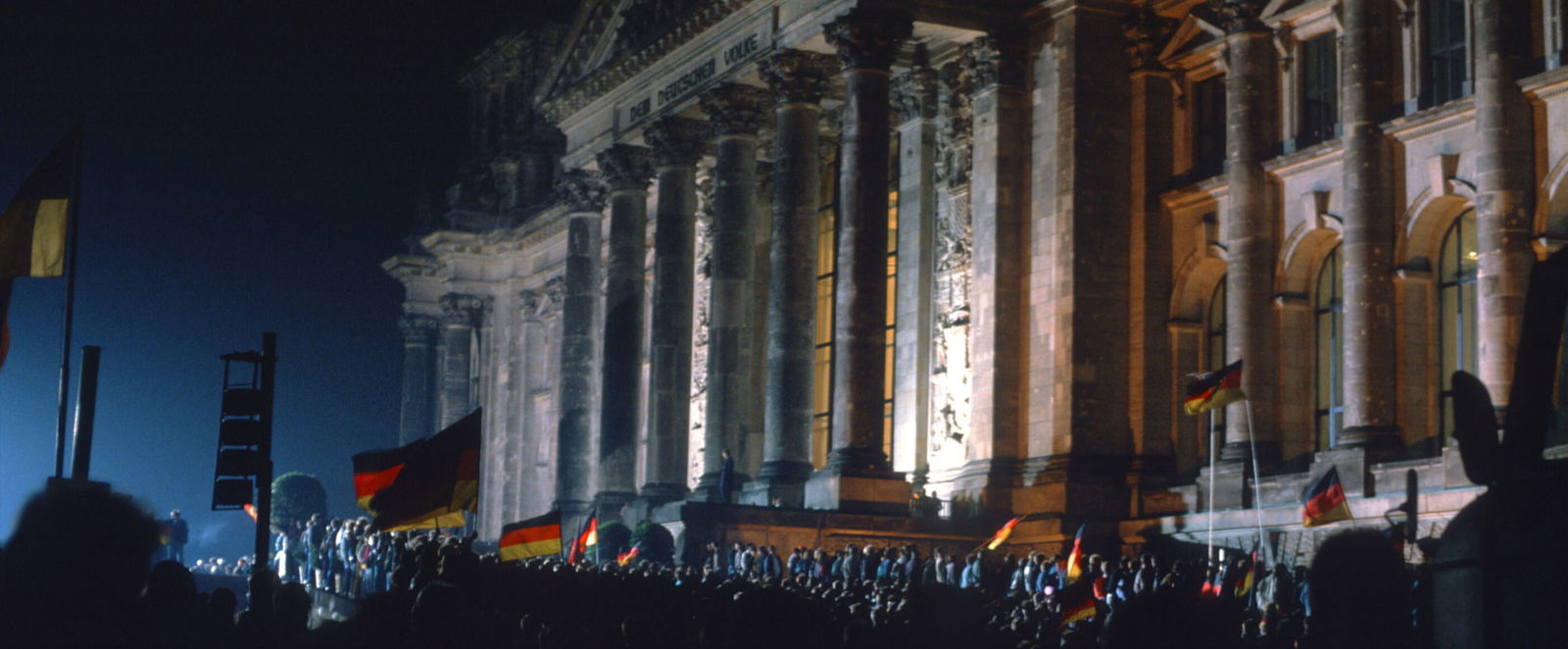 Viele Menschen im Dunkeln vor dem Brandenburger Tor, mit Deutschlandfahnen.