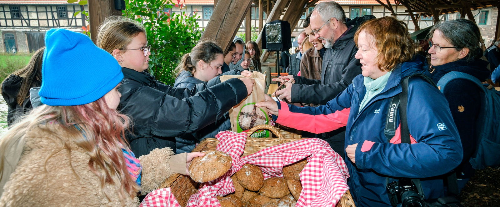 Zwei jüngere Menschen geben Brötchen aus Körben an andere Menschen aus.