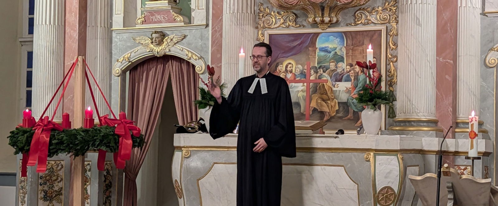 Eine männlich gelesene Person im Talar steht vor dem Altar in einer Kirche.