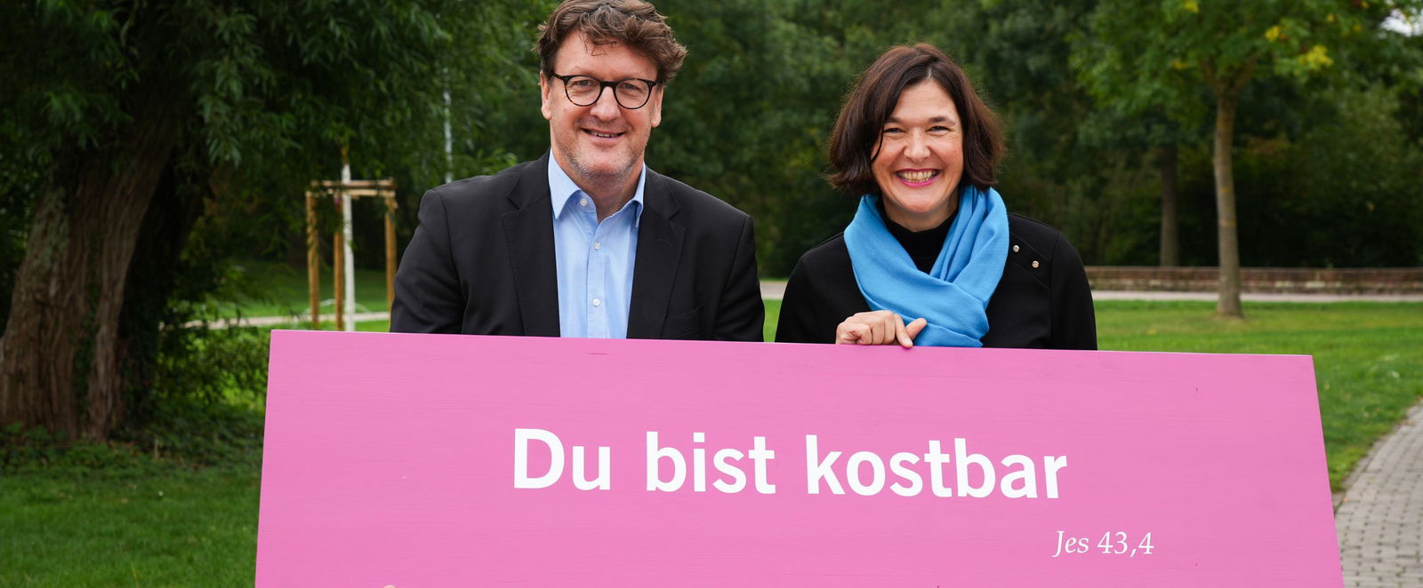 Zwei Menschen halten ein pinkes Schild.